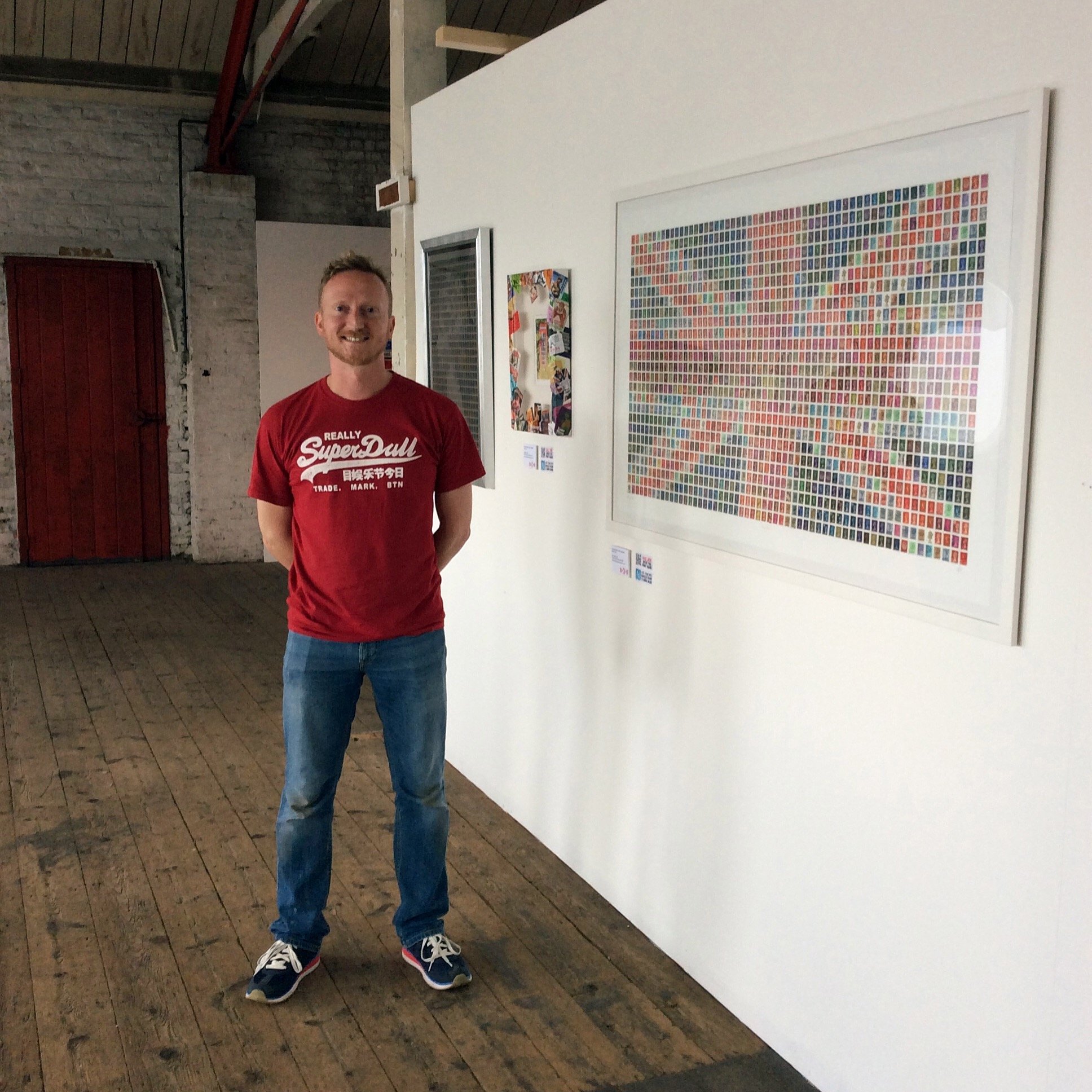 Exhibition install, standing beside the large framed postage stamp collage